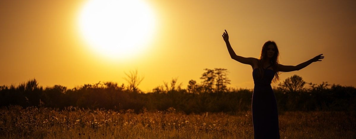 A woman dances in a meadow at sunset.