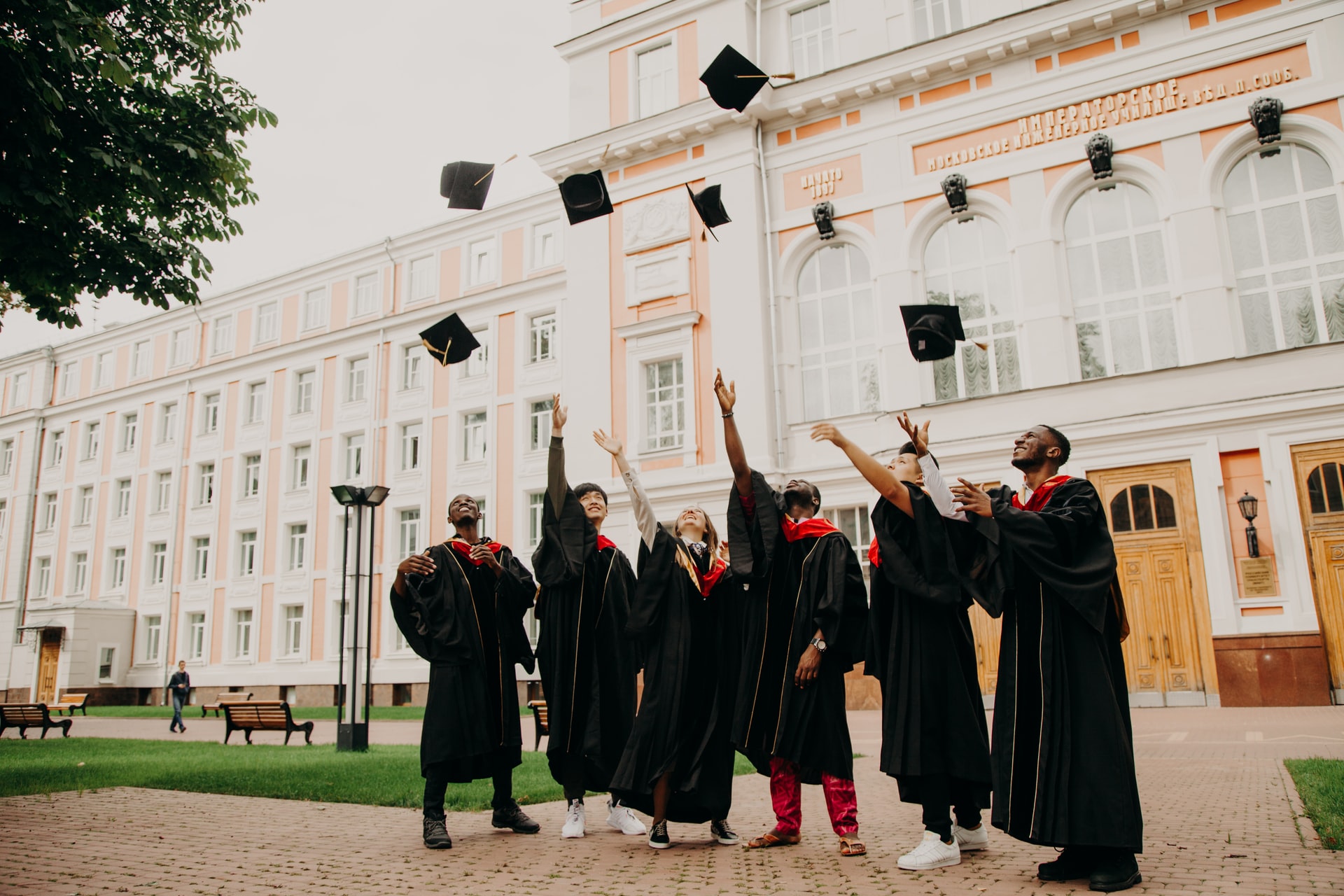 A group of graduates tosses their caps in the air in front of an academic building
