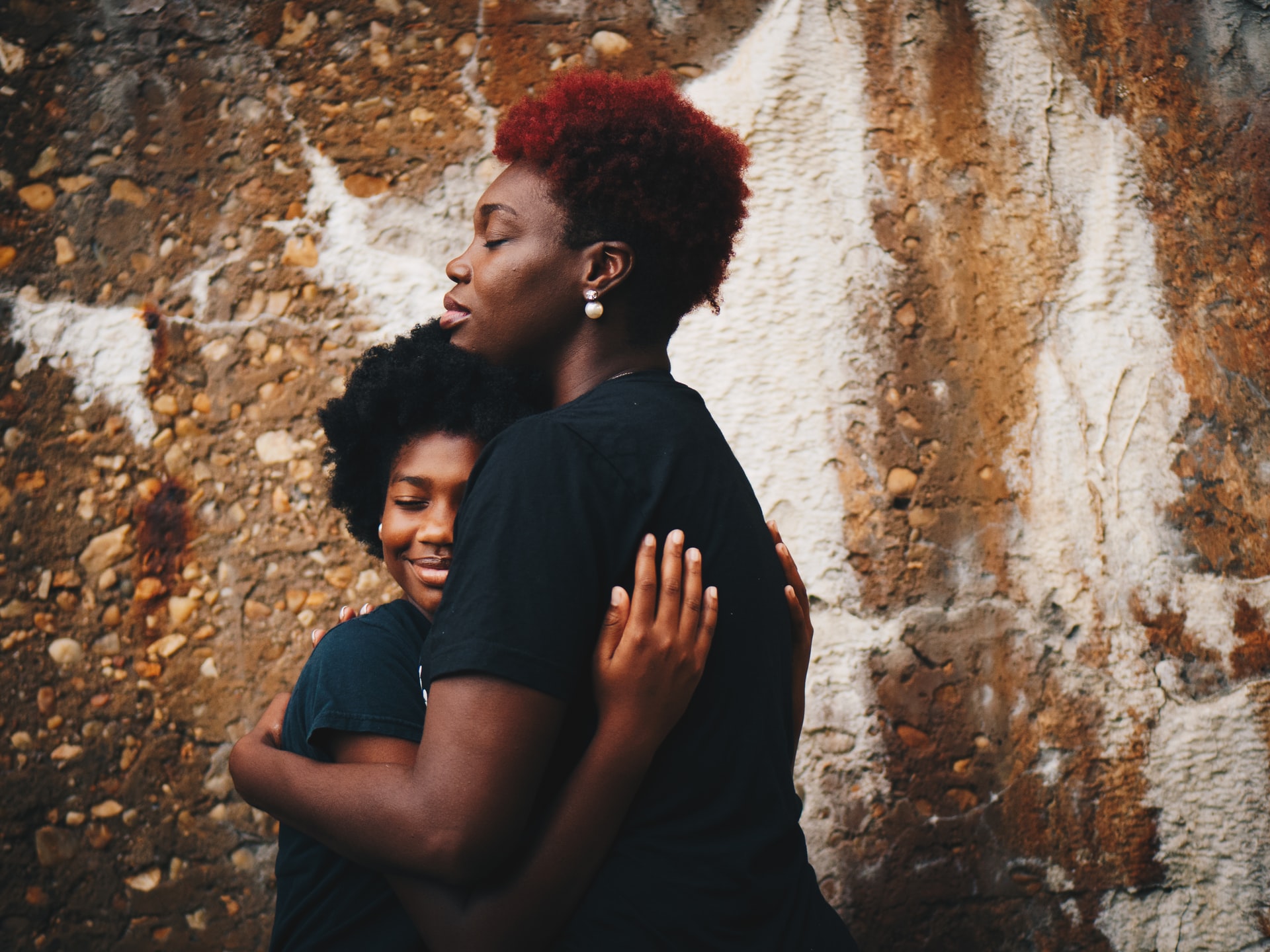 Teenager and mother hug in front of stone wall