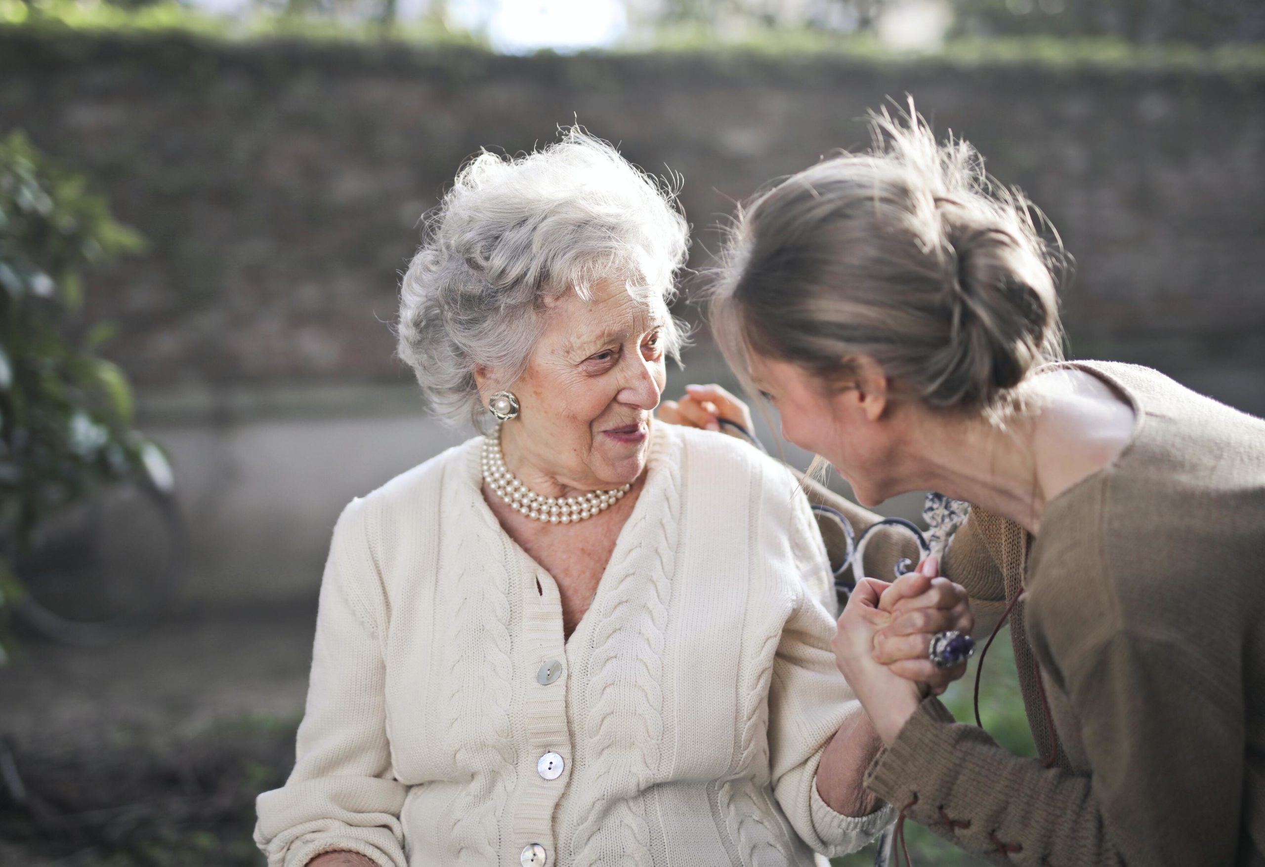 A young woman talks closely with a senior woman who is smiling.