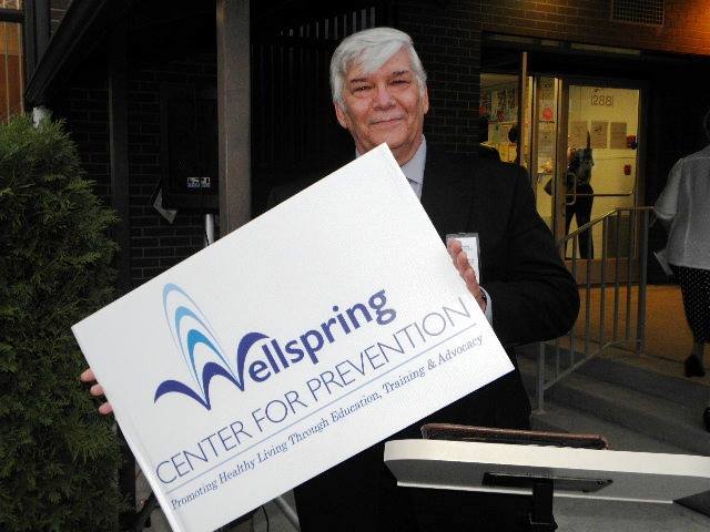 Ezra Helfand holding a posterboard with Wellspring's new name and logo.