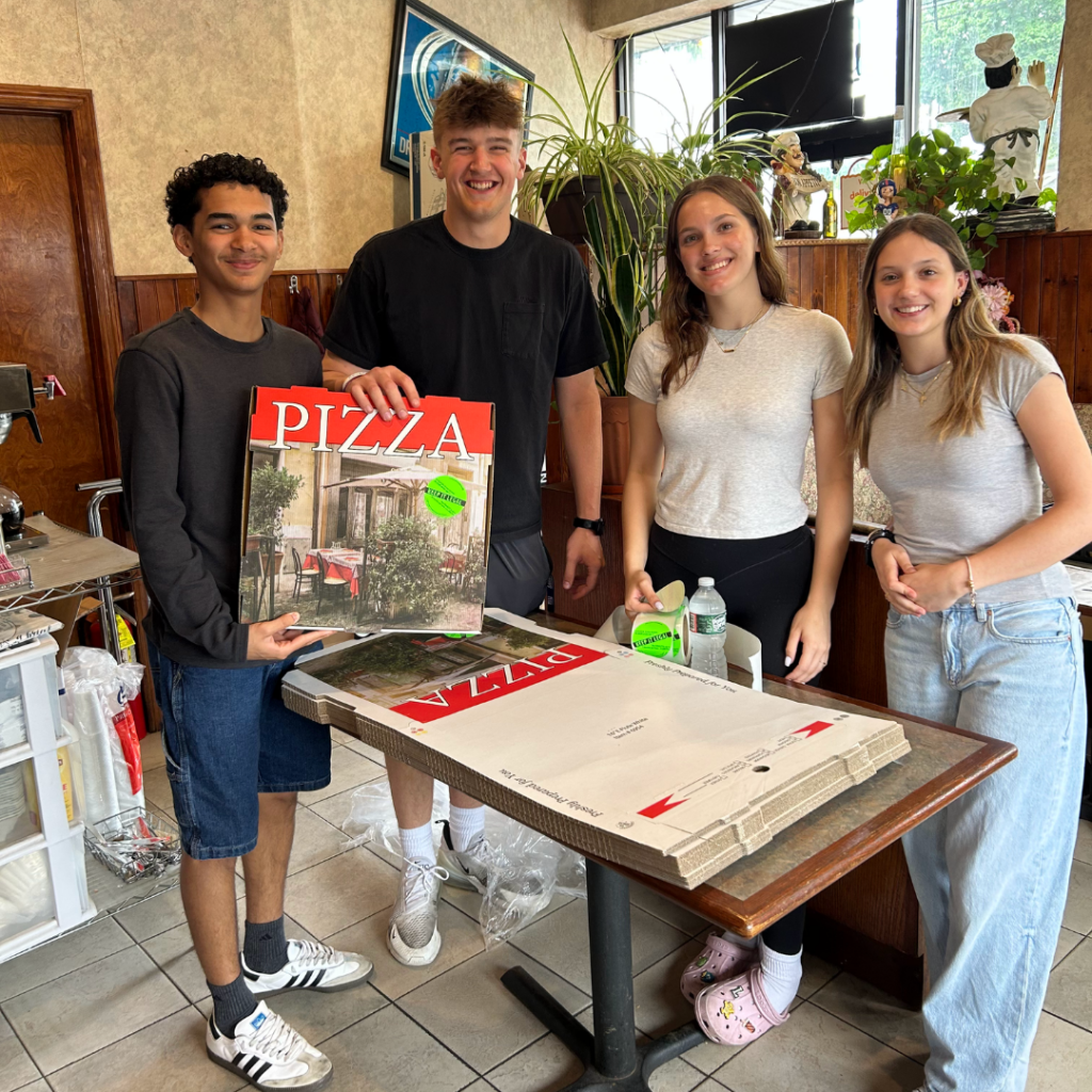 teens posing for photo with pizza boxes