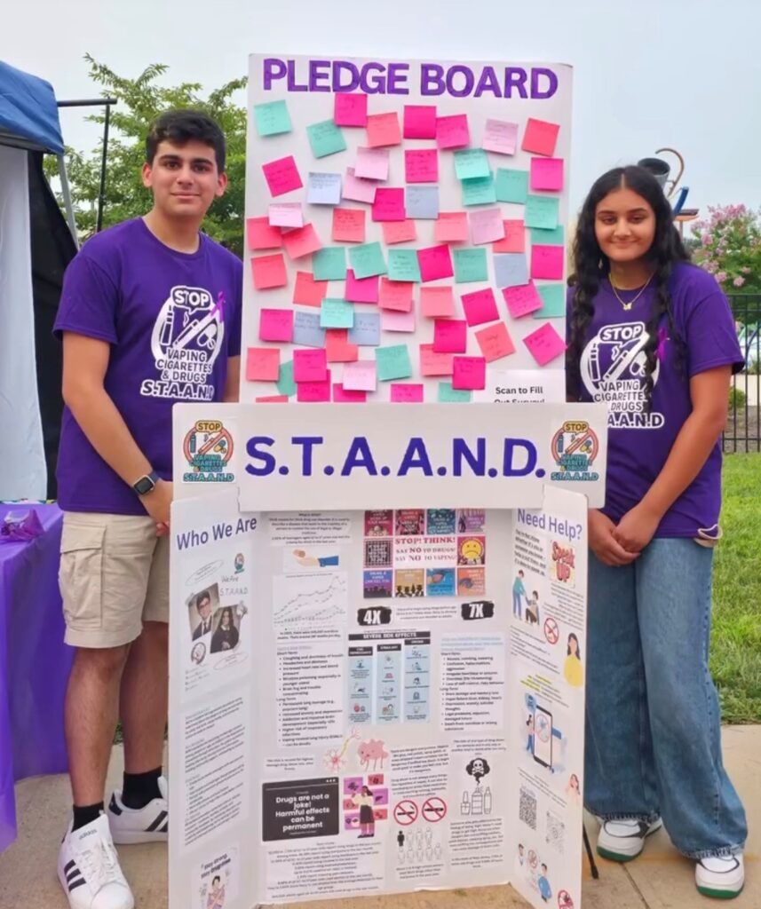 Piscataway High School students Ayush Desai and Devi Patel stand beside a S.T.A.A.N.D pledge board at a community event, promoting teen vaping and substance use prevention.