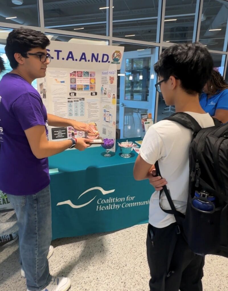 Ayush Desai demonstrates vaping health risks to a student at a Coalition for Healthy Communities event, part of a teen-led substance use prevention initiative.