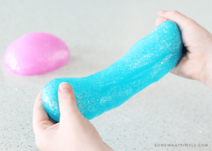 Hands stretching bright blue slime with a pink slime ball in the background.