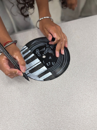 Student painting a vinyl record with black and white designs during an arts and crafts activity.