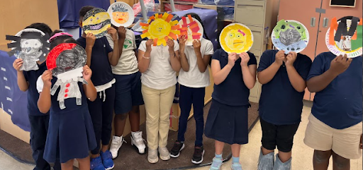 A group of elementary school students hold up colorful handmade art projects during the Pathways Summer Program.